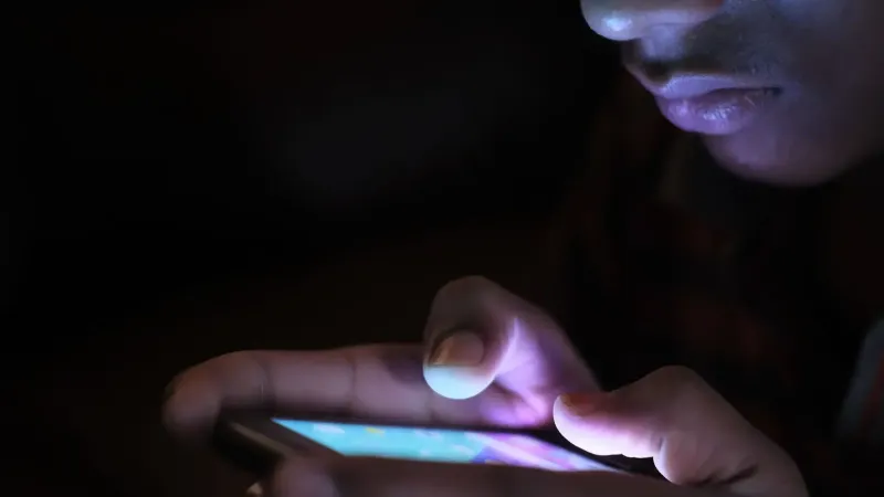 Close-up of a person holding and using an illuminated smartphone in a dark setting.