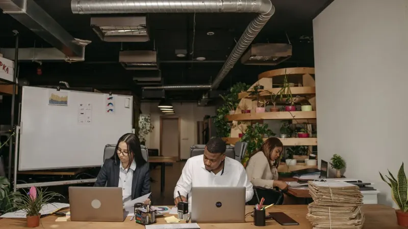 Three professionals focused on work in a stylish office with laptops and documents.