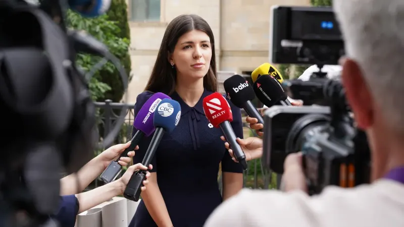 Un portavoz se involucra con los medios durante una entrevista de prensa al aire libre rodeada de micrófonos.