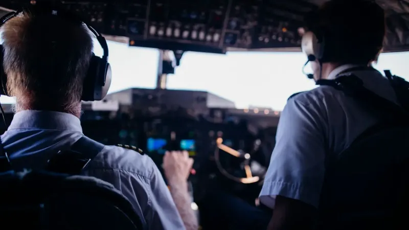 Vista trasera de pilotos masculinos anónimos en uniforme y auriculares navegando por un avión moderno mientras despega