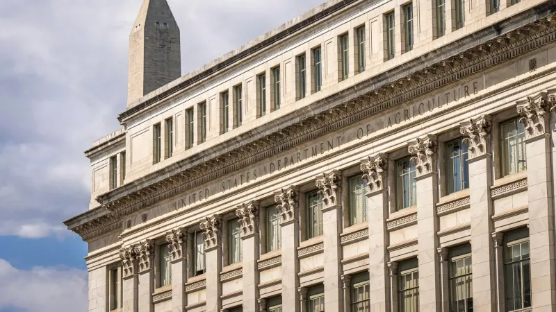 US Department of Agriculture building with Washington Monument behind, blue sky with clouds.