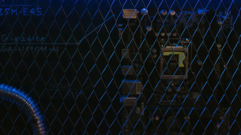 Artistic view of a circuit board through metal mesh with blue lighting.