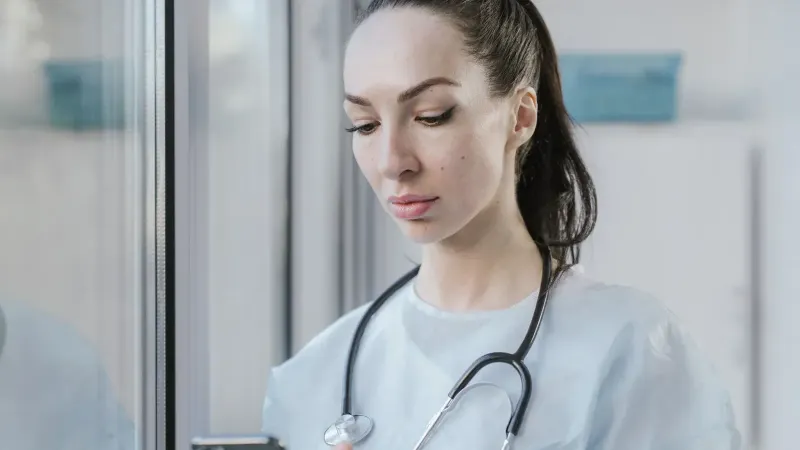 Portrait of a female doctor in a disposable gown using a smartphone in a hospital environment.