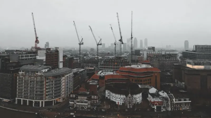 Foggy day in London featuring construction cranes over the cityscape in a moody atmosphere.