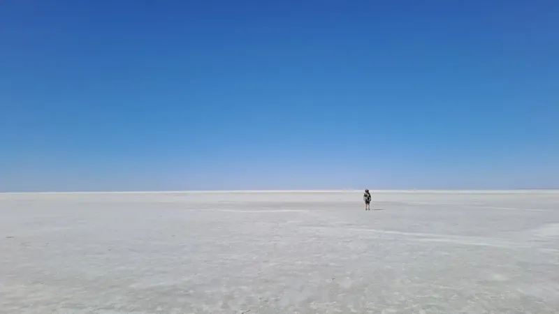 A lone traveler explores the expansive salt flats under a clear blue sky in South Australia.