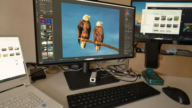 A desk setup showing photo editing software on multiple monitors, a keyboard, and peripherals.