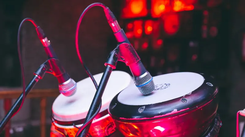 A close-up view of bongo drums with microphones on stage, illuminated by dynamic red lighting.