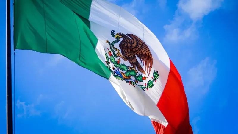 Vibrant Mexican flag waving in the clear blue sky, symbolizing national pride.