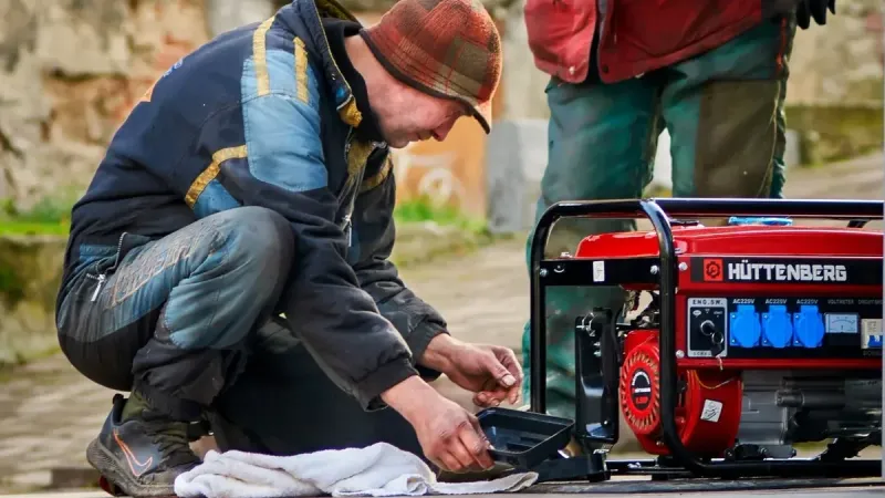 Two technicians working on a red HÜTTENBERG power generator outdoors.