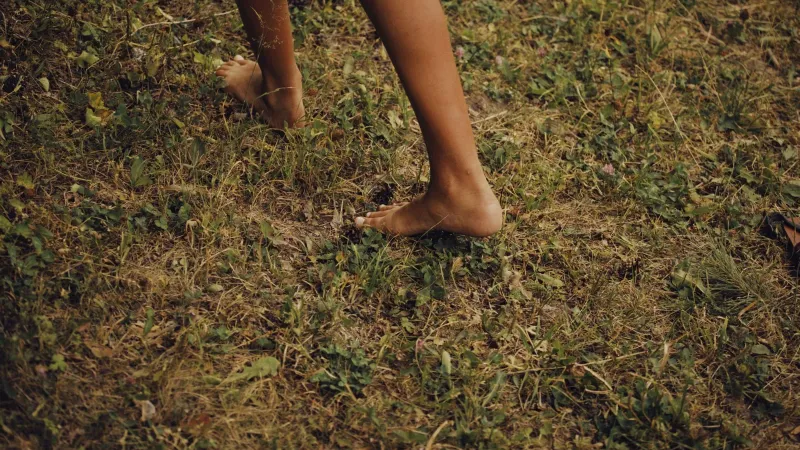 Close-up of bare feet walking on grassy ground, embodying a natural outdoor experience.