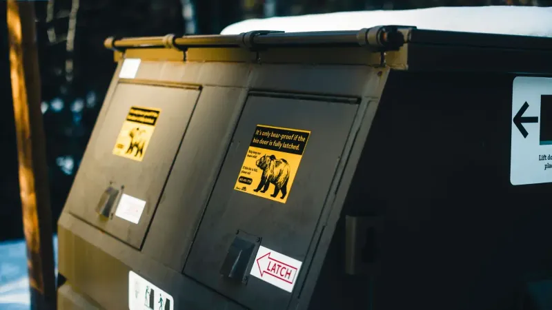 Close-up of bear-proof dumpster with warning signs, emphasizing wildlife safety in Canada.