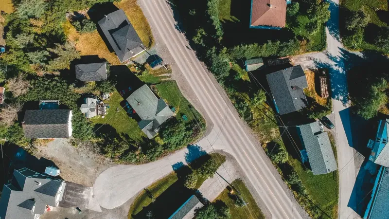 Aerial top view of house rooftops on green valley land with roadway in remote rural village