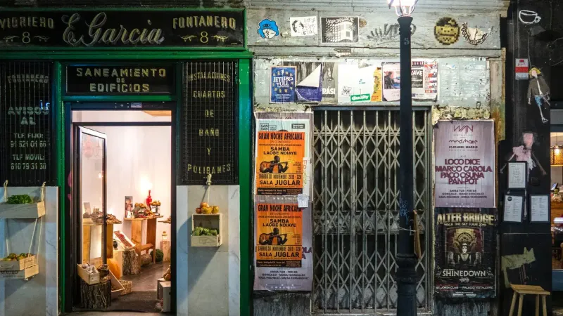 Charming vintage storefront with warm interior lighting and colorful street posters at night.