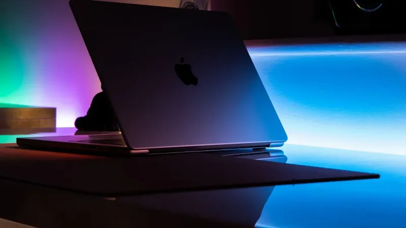 A MacBook reflecting vibrant neon lights in a dimly lit room setting.