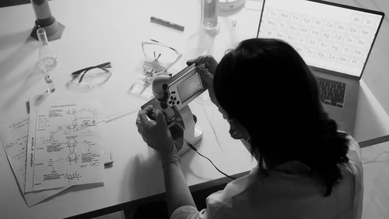 Researcher conducts experiments using a microscope in a monochrome lab setting.