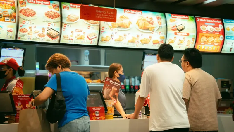Clientes que piden comida en un mostrador de restaurante de comida rápida. Ambiente ocupado.