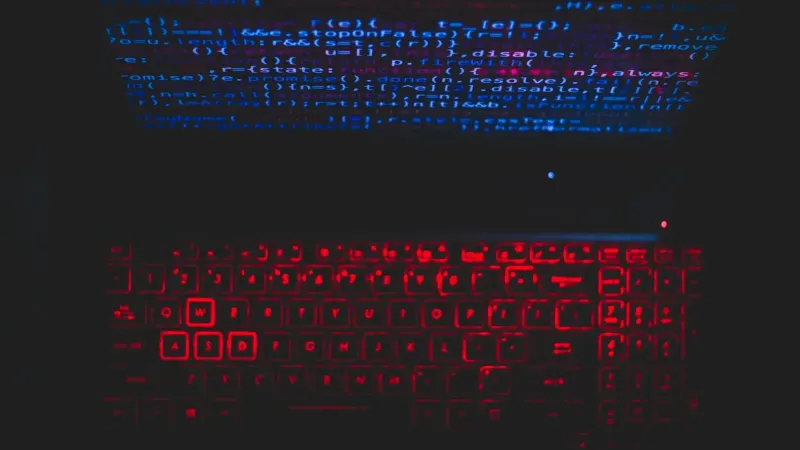 Dark-themed laptop setup with a red glowing keyboard and code on screen, ideal for tech enthusiasts.
