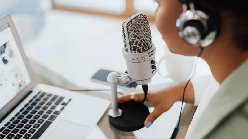 Professional woman recording a podcast or broadcast using a microphone and laptop at a desk.