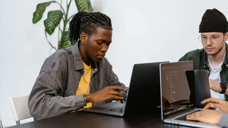 Two young adults working together on laptops in an office setting, focusing on tasks.