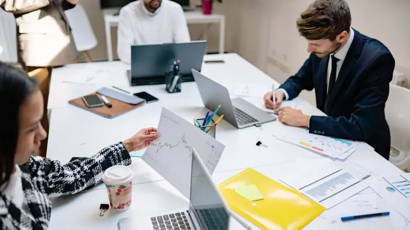 Professionals collaborating in a modern office with laptops and documents, focusing on teamwork.