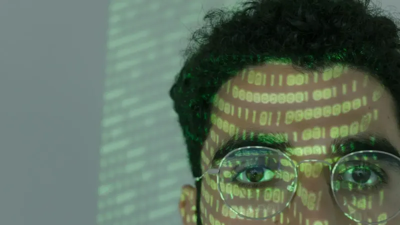 Close-up of a man with binary code projected on his face, symbolizing cybersecurity.