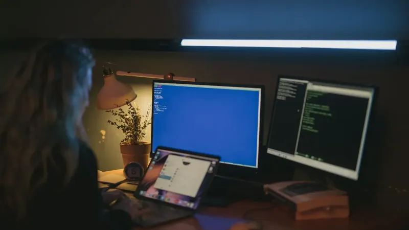 Woman using multiple screens for cybersecurity tasks in a cozy home office