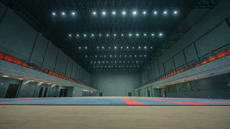 Spacious indoor sports hall with bright ceiling lights and empty flooring in Surat, India.