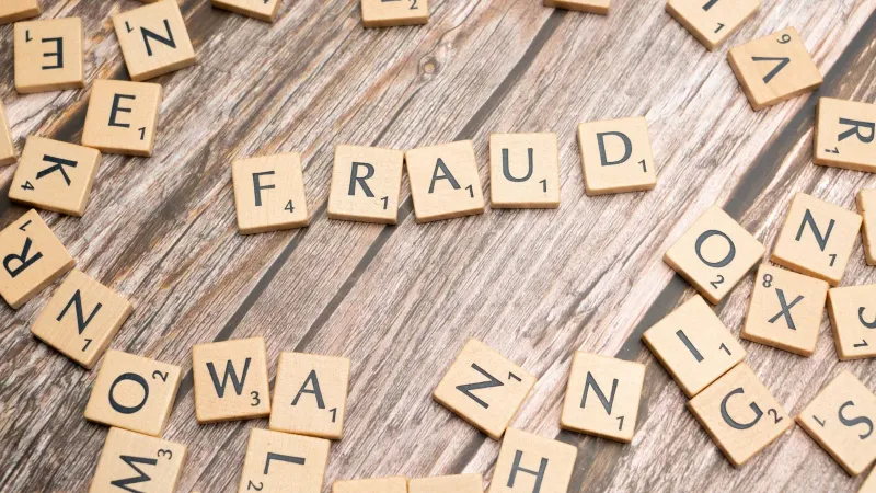 Alphabet tiles arranged to spell 'fraud' on a wooden surface, symbolizing deception.