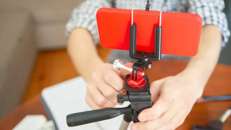 Close-up view of a person setting up a smartphone on a tripod indoors.