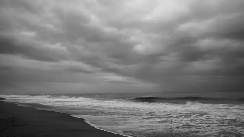 Una espectacular escena de playa en escala de grises con cielos nublados que levantan las olas del océano.