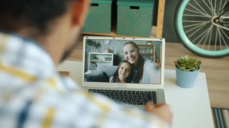 A person video calling with family, showing mother and child on the laptop screen.