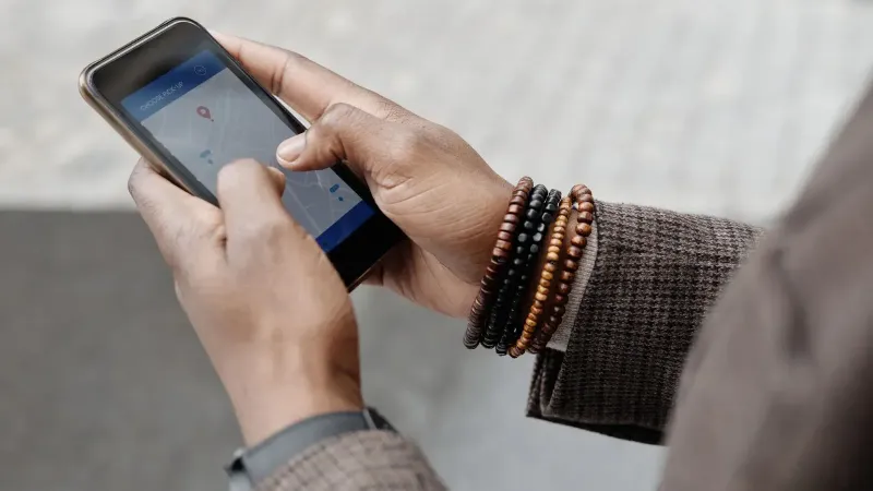 Close-up de manos con pulseras navegando en smartphone usando la aplicación GPS al aire libre.