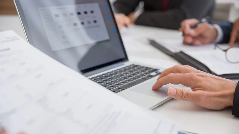 Close-up of hands working on documents and a laptop in an office setting, illustrating teamwork and productivity.
