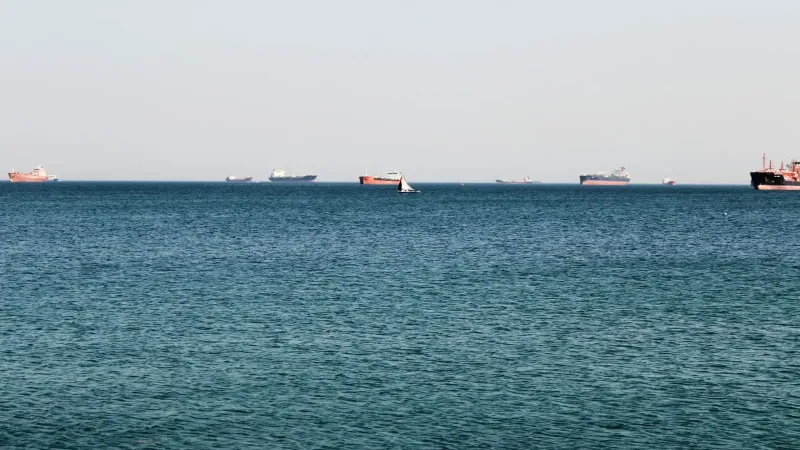 Una tranquila vista al mar con varios buques de carga en el horizonte bajo un cielo despejado.