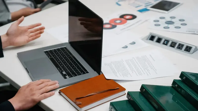 Primer plano de una mesa de reuniones de negocios con una computadora portátil, documentos y discusión en curso.