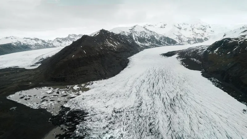 Stunning aerial view of a vast glacier surrounded by snow-capped mountains and icy terrain.