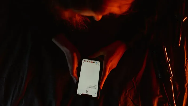 A person using a smartphone in dim, moody lighting with a dark background.