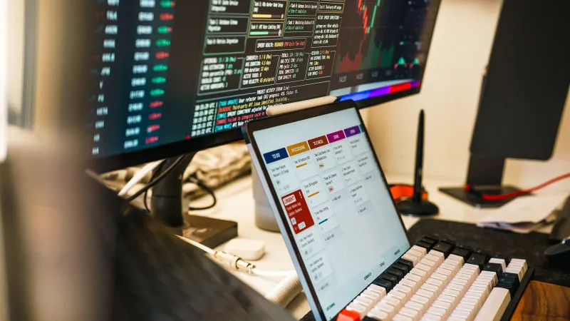 A sleek, modern workspace featuring trading monitors and a tablet for project management.