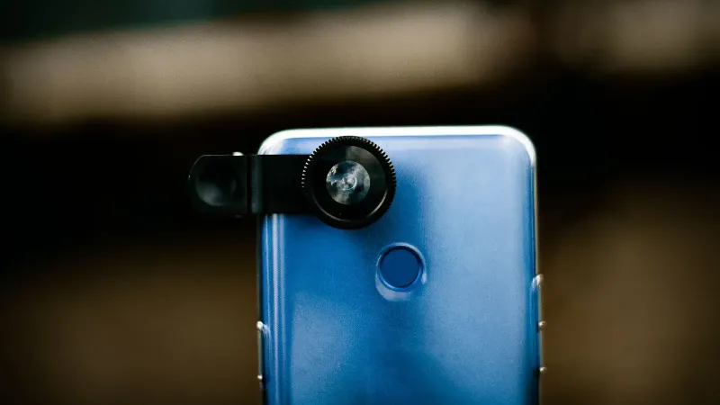 Zoom optical lens attached to camera of modern smartphone against blurred background in daytime