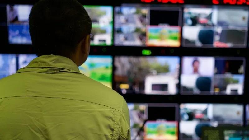 Man in a control room overseeing multiple monitors displaying various scenes.