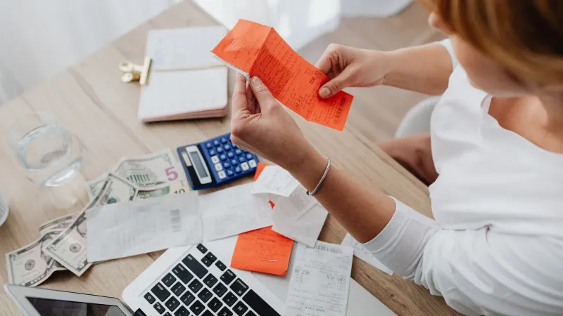 Woman using calculator and receipts at home office desk for finance management.