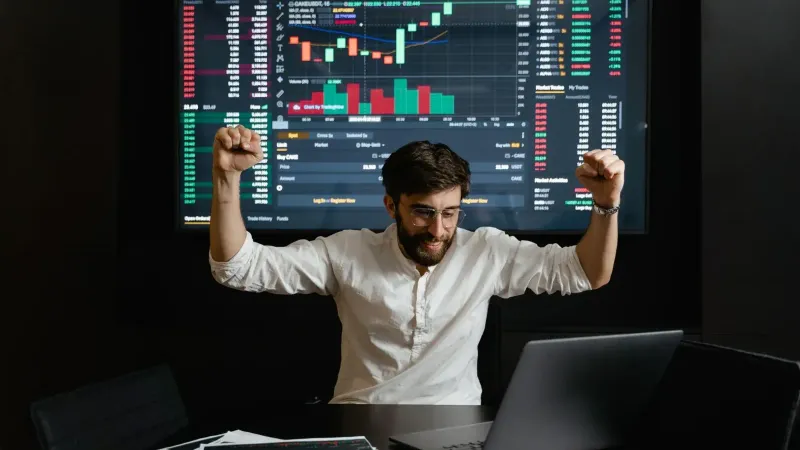 El empresario celebra el éxito del mercado de valores con las manos levantadas de emoción en una mesa de negociación.