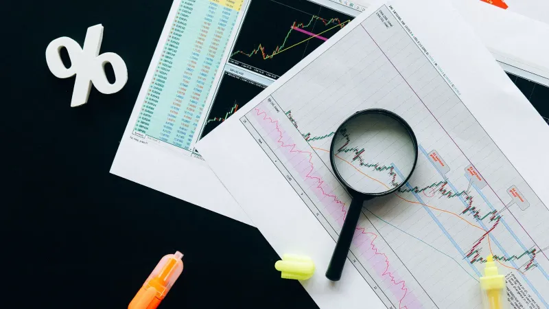 High-angle view of financial charts, showcasing stock market analysis with magnifying glass and highlighters.