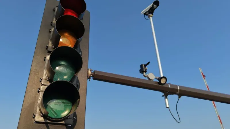 Urban scene with a traffic light and CCTV camera against a clear blue sky.