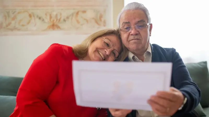 An elderly couple happily reviews a document while sitting comfortably together on a sofa.