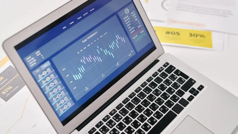 Open laptop displaying financial graphs and analytics with documents nearby, ideal for business presentations.
