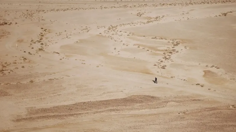 Una figura solitaria camina a través de un vasto paisaje desértico, enfatizando la soledad y la extensión de la naturaleza.