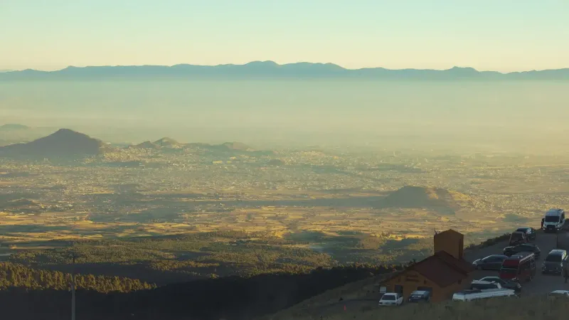 Aerial view of a city in a valley, with smog and distant mountains creating a serene landscape.