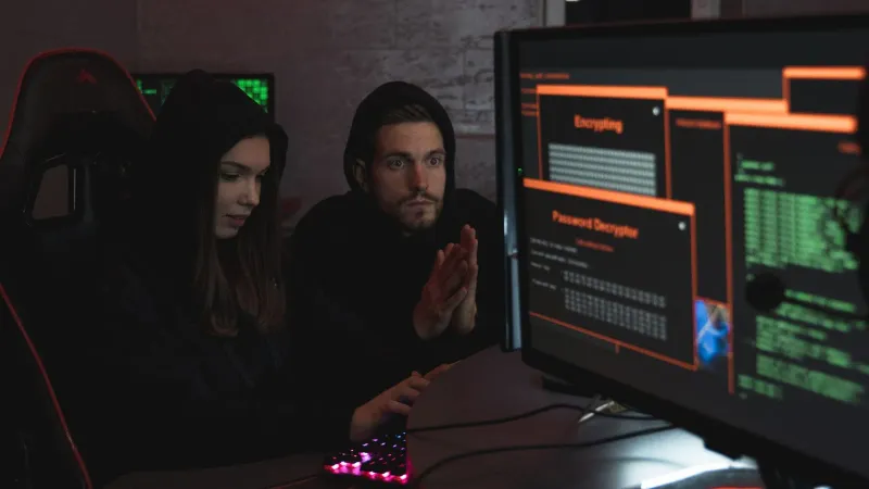 Cybersecurity experts in hoodies analyzing encrypted data on computer screens in an indoor setting.