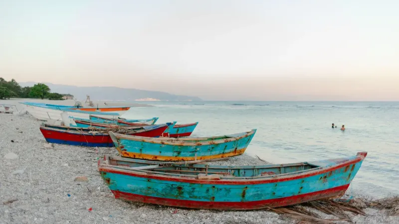 Shabby wooden fishing boats moored on pebble coast near travelers swimming in rippling sea in evening